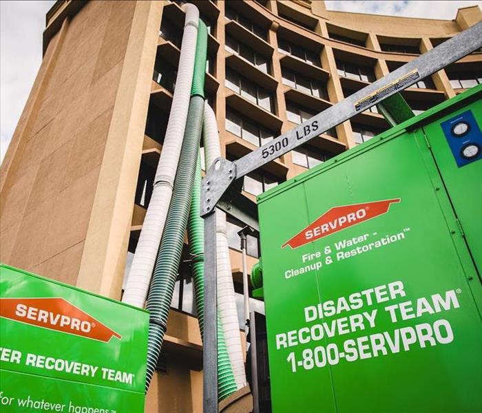 SERVPRO industrial-grade dehumidifiers and air movers parked outside of a hotel with air tubes rising up multiple stories
